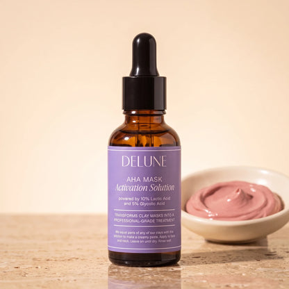 Solução ativadora AHA para máscaras Delune, frasco conta-gotas de 30 ml, sobre travertino ao lado de um pote com pasta de argila rosa