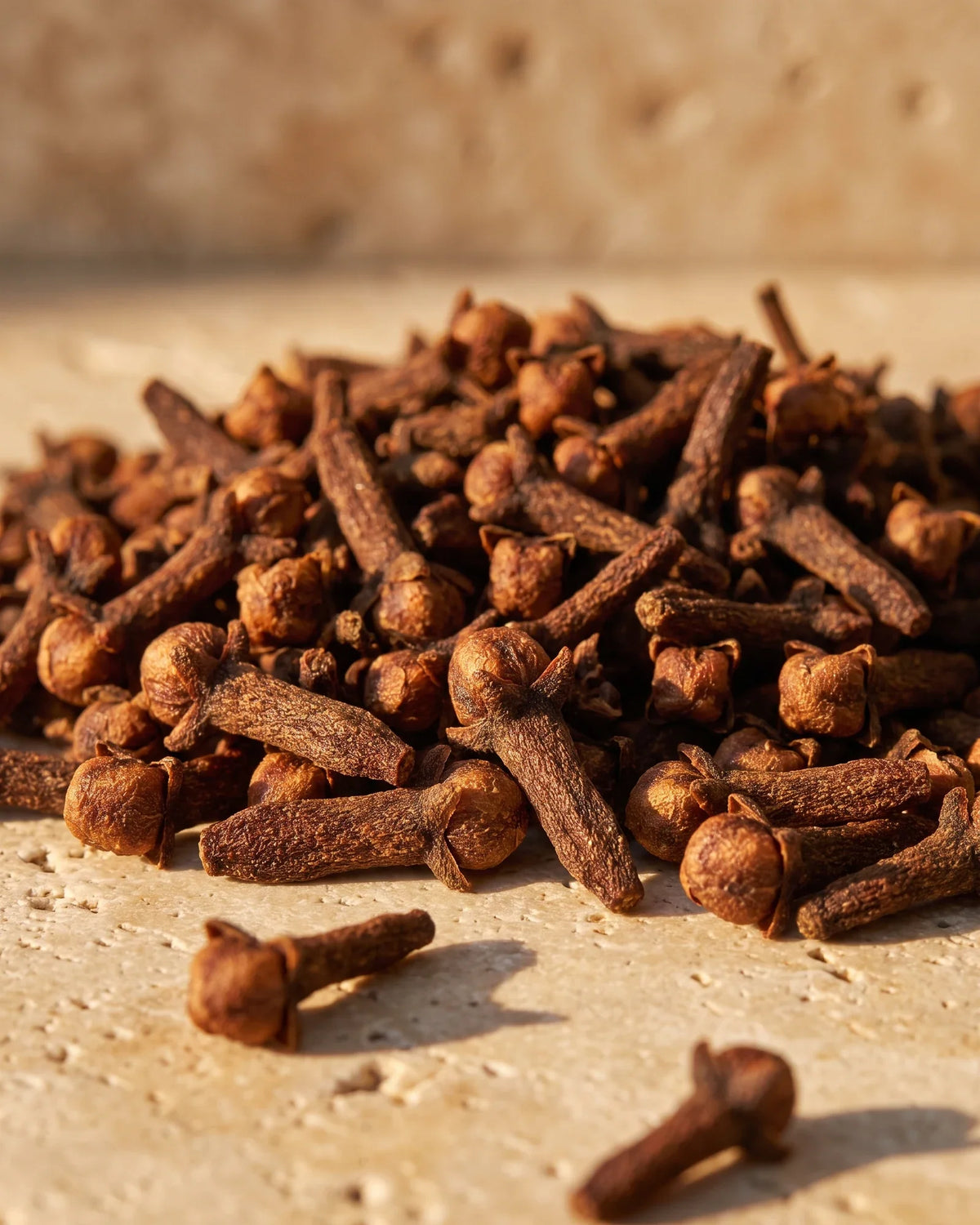 Um punhado de cravos-da-índia secos sob luz quente e rasante sobre travertino — o aroma quente e especiado do Óleo essencial puro de cravo Delune
