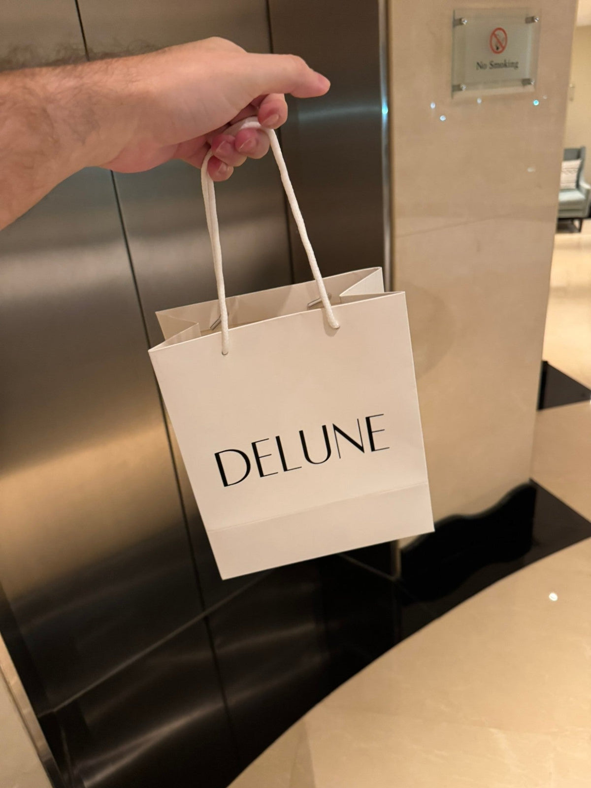 Uma mão segurando uma sacola de presente branca da Delune, a caminho de entregar um pedido