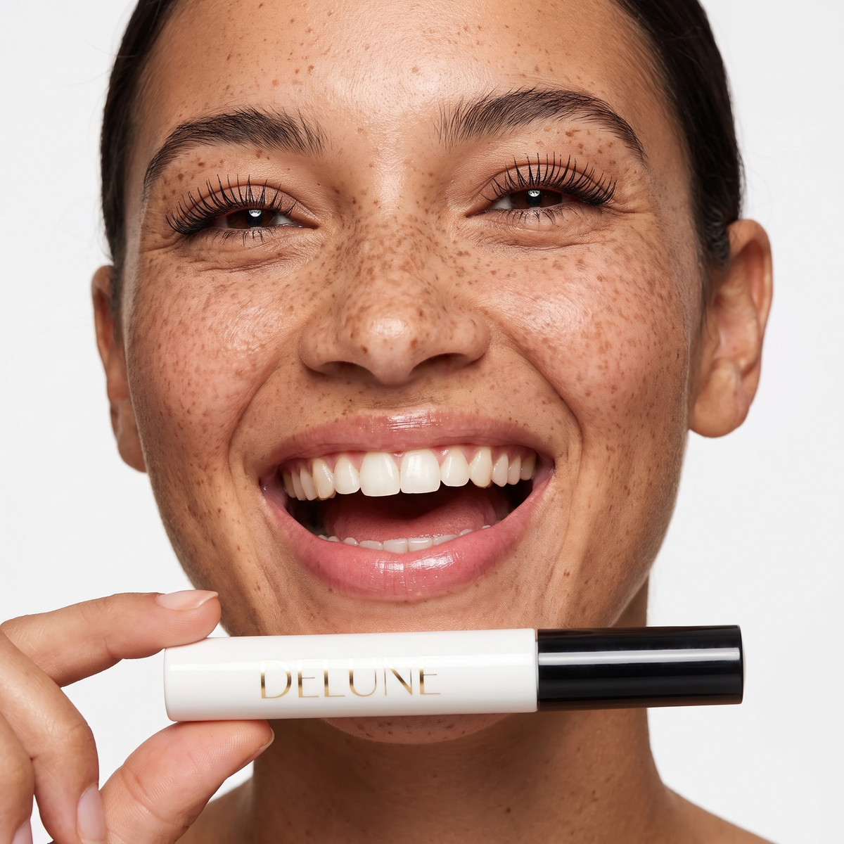 Delune Tubing Mascara, model laughing with lifted lashes, holding the white tube