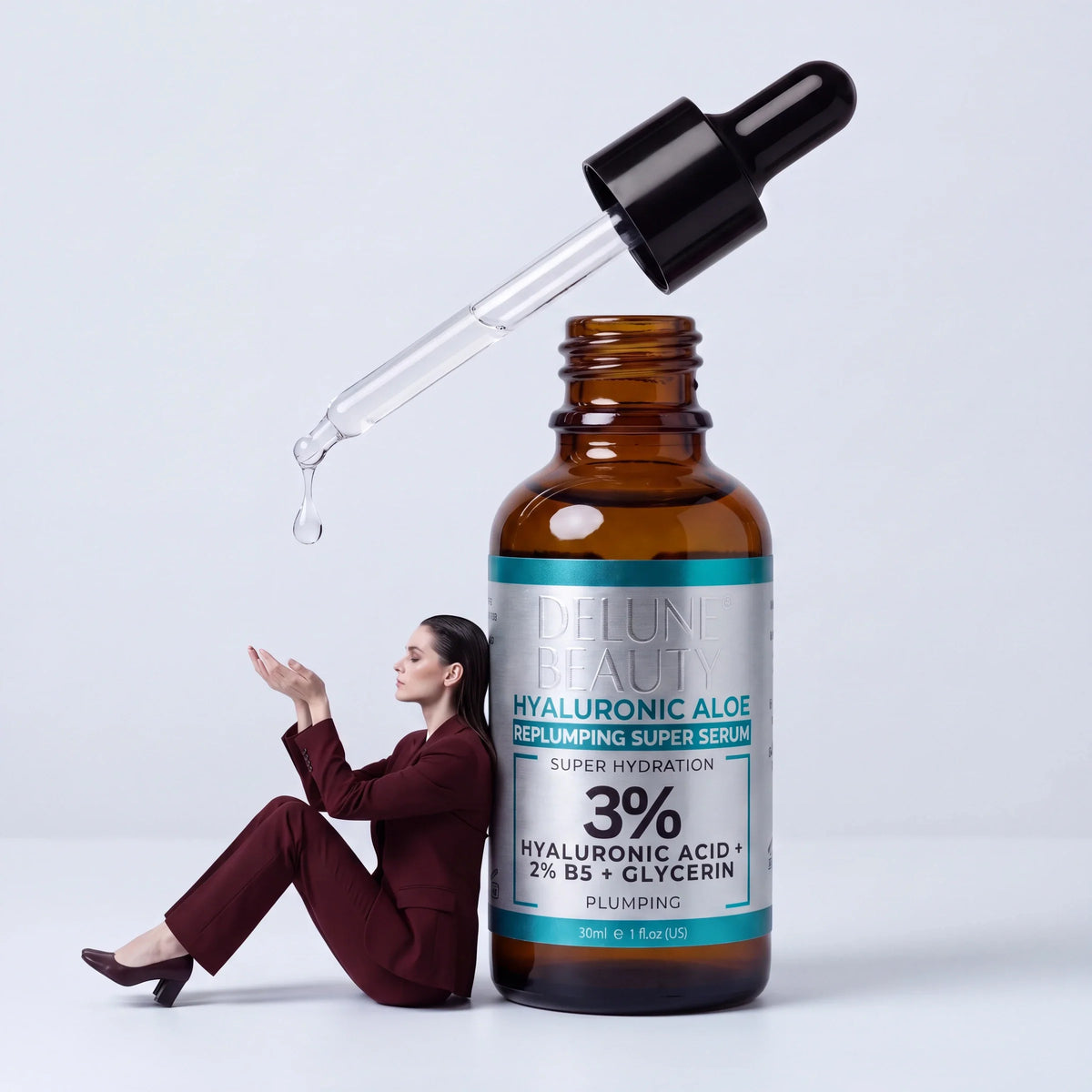 Restaurar: uma mulher de terno bordô apoiada em um sérum Hyaluronic Aloe Delune gigante, pegando uma gota que cai